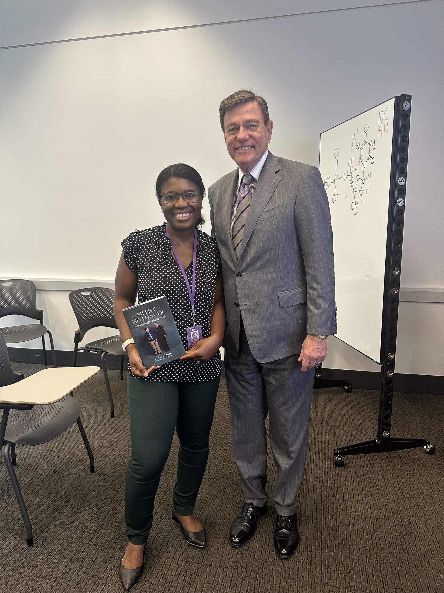 Robert Stack stands beside Professor Dora Onwumere at New York University; she holds a copy of “Silent No Longer” as they pose together indoors following a guest lecture.